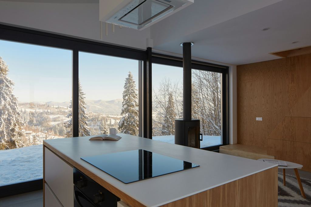 Modern kitchen island in front of floor-to-ceiling windows with a snowy forest view